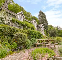 An outdoor garden area with a wooden picnic table and a stone house covered in plants at Llety Perygl in Harlech