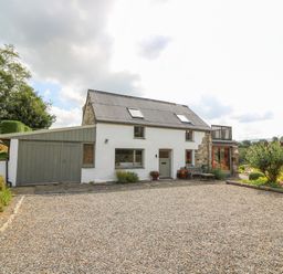 A white house with a garage and gravel driveway surrounded by trees and garden at Plasybangor Newport Pembrokeshire