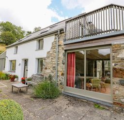 Exterior view of a stone and white plaster cottage with patio furniture and upper balcony at Plasybangor in Newport Pembrokeshire