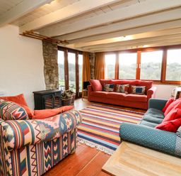 A living room with three sofas a striped rug a wood stove and large windows at Plasybangor in Newport Pembrokeshire