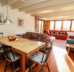 A living room with a wooden dining table and black chairs and sofas with patterned cushions at Plasybangor in Newport Pembrokeshire