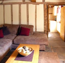A living room with a brown sectional sofa a wooden coffee table with a bowl of decorative balls and exposed wooden beams on walls at Point Cottage in Preston-on-Wye near Hereford