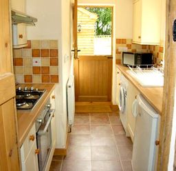 A narrow kitchen with stove oven microwave washing machine and sink at Point Cottage Preston on Wye near Hereford