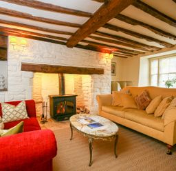 A sitting room with exposed wooden beams a stone fireplace two sofas and a coffee table at Murton Cottage in Burford