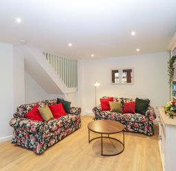 A living room with floral sofas red and green pillows a round wooden coffee table and a white shelving unit at The Forge in Shipham
