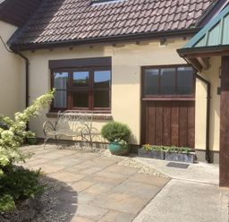A paved courtyard with a metal bench plants and a building with tiled roof and windows at The Forge in Shipham