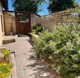 A paved garden path with plants and wooden fencing at Mendip Cottage in Shipham