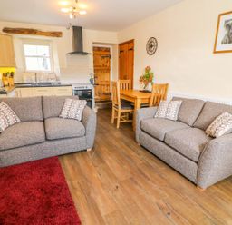 A living room with two sofas a wooden dining table a kitchen area and wooden doors at Tilberthwaite Farm Cottage in Coniston