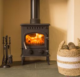 A wood burning stove with fire inside and a basket of firewood next to it at Tilberthwaite Farm Cottage in Coniston