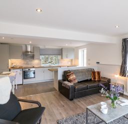An open plan living room and kitchen with a black leather sofa and a dining table at Cuckoo Cottage in Bridport