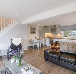 An open plan living room and kitchen with a black leather sofa and dining table at Cuckoo Cottage in Bridport
