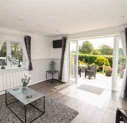 A living room with a coffee table and flowers by a window and sliding doors opening to a garden at Cuckoo Cottage in Bridport