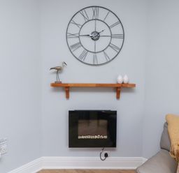 A living room featuring a clock, shelf, and electric fireplace at Hasting Dairy in North Sunderland near Seahouses
