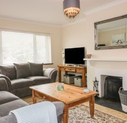 A living room with grey sofas a wooden coffee table a fireplace and a television at Dune Haven in Goonhavern near Perranporth