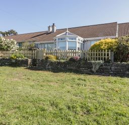Exterior of a single-story house with a brown tiled roof garden with shrubs picket fence and grass lawn at Dune Haven in Goonhavern near Perranporth