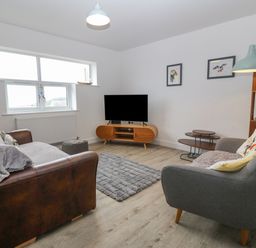 A living room with two sofas a television on a wooden stand and a floor lamp at Cysgod Y Capel in Benllech