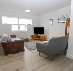 A living room with two sofas a television on a wooden stand a highchair and a floor lamp at Cysgod Y Capel in Benllech