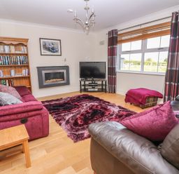 A living room with pink sofas a wooden bookshelf a flat screen tv and a window with striped curtains at Cadwgan in Aberporth