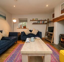 A living room with blue sofas a wooden coffee table a fireplace and bookshelves at Swallows Nest in Morvah