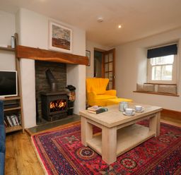 A living room with a fireplace a yellow armchair a wooden coffee table and a television at Swallows Nest in Morvah