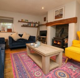 A living room with blue sofas a yellow armchair and a wooden coffee table on a patterned rug at Swallows Nest in Morvah