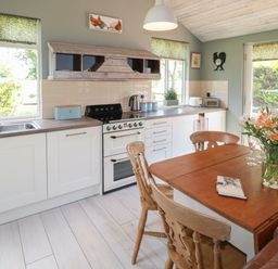 A kitchen with wooden dining table and chairs with flowers on the table at The Hen House in Stockwell Heath near Rugeley