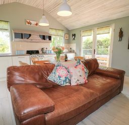 A kitchen and living area with a brown leather sofa and floral cushions at The Hen House in Stockwell Heath near Rugeley