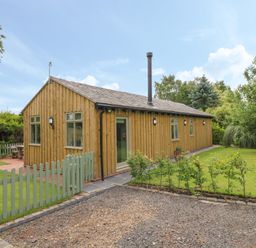 A wooden cabin with multiple windows surrounded by green lawn and a small green fence at The Hen House in Stockwell Heath near Rugeley