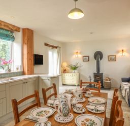A kitchen dining area with a wooden table set with floral dishware a stove and a wooden cabinet at The Old Laundry in North Tawton