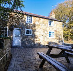 An outdoor area with a stone house and patio furniture at Woodland Cottage in Garth