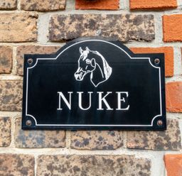 A black sign with a horse head illustration and the word nuke mounted on a brick wall at Nuke in Weymouth