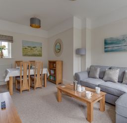 A living room with a gray sofa wooden coffee table dining table with chairs bookshelf and paintings at Nuke in Weymouth