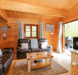A wooden living room with two brown leather sofas a wooden coffee table a flat screen tv and a door opening to an outdoor area with a barbecue at Heron Lodge in Badwell Ash