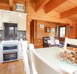 A wooden interior kitchen and living area with white cabinets brown leather sofas and a dining table at Heron Lodge in Badwell Ash
