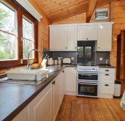 A kitchen with white cabinets a stove a sink and large windows at Heron Lodge in Badwell Ash