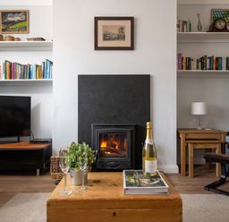 A living room with a wood burning stove bookshelves a television and a wooden coffee table at Heddfan in Conwy