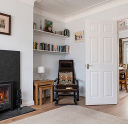 A sitting area with a chair and nested tables next to a fireplace and bookshelves at Heddfan in Conwy