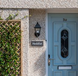 A blue door with the number 30 and a plant on a wooden trellis beside it at Heddfan in Conwy