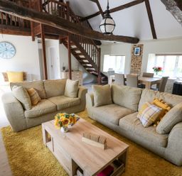 A living room with beige sofas and a wooden coffee table on a yellow rug at Far Barn in Fakenham