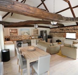 An open plan kitchen and living room with wooden beams a dining table with chairs beige sofas and a television at Far Barn in Fakenham