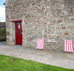 Two chairs and a table in front of a stone wall at Milking Shed near Narberth