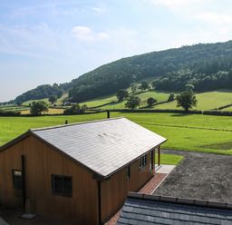 A wooden house with a slate roof near green fields and hills at Meadow View in Meifod Powys