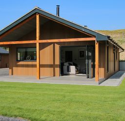 A brown wooden house with a covered patio and lawn at Meadow View in Meifod Powys