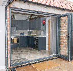 A kitchen with dark cabinets, a washing machine, oven, toaster, and open folding glass doors at Owl View in Lebberston near Cayton