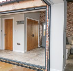 An open doorway showing an interior space with wooden doors tile flooring a coat rack and a gray sofa against a brick wall at Owl View in Lebberston near Cayton