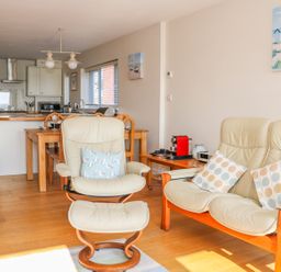 A living room with cream leather armchairs and wooden dining table at Harbour View Mudeford in Christchurch