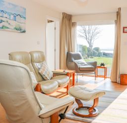 A living room with leather chairs and a footstool facing a large window and door to a garden at Harbour View Mudeford in Christchurch