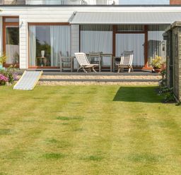 A backyard with wooden deck chairs a table a shed plants and a lawn at Harbour View Mudeford Christchurch