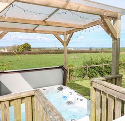 An outdoor hot tub under a wooden pergola with string lights and a view of fields at Mountain View Lodge Tavernspite near Narberth