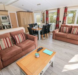 A living room with two brown sofas a wooden coffee table and a dining table with six black chairs at Mountain View Lodge Tavernspite near Narberth